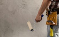 Construction worker man holding paint roller tool near wall. Mal